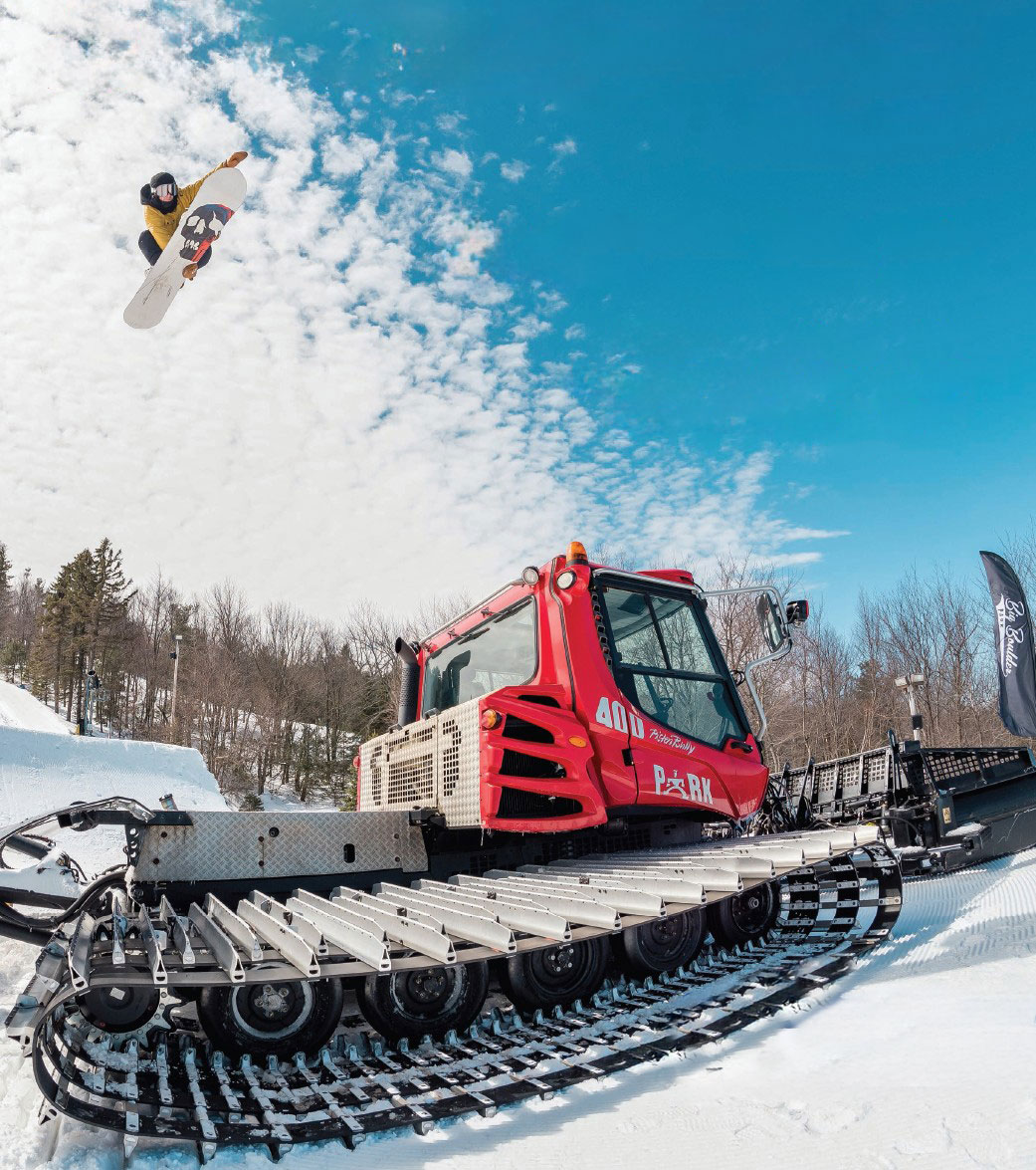Snowboarder jumping over snow grooming machine