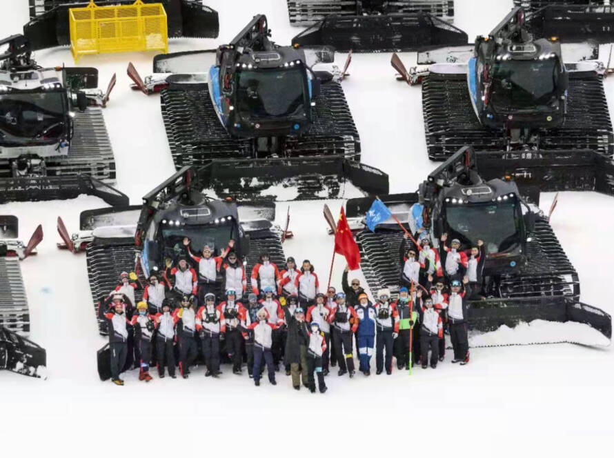 Aerial view of group of people waving, standing in front of rows of snow grooming machines