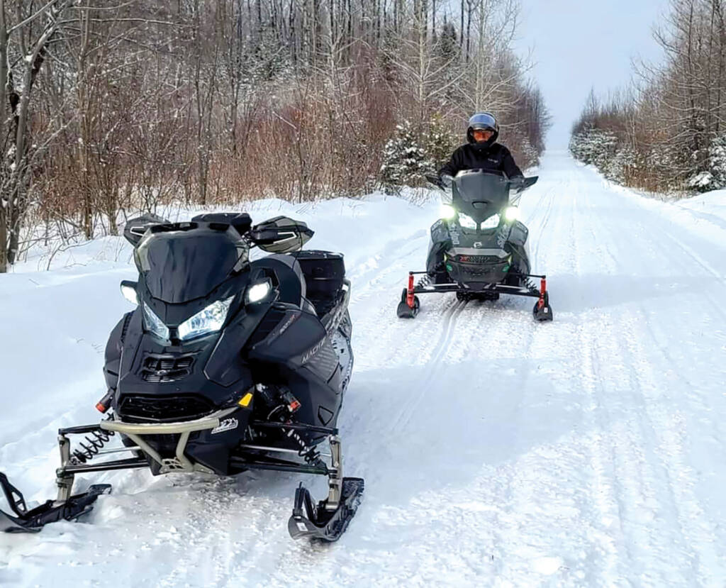 Two snowmobiles on trail. One sitting idle
