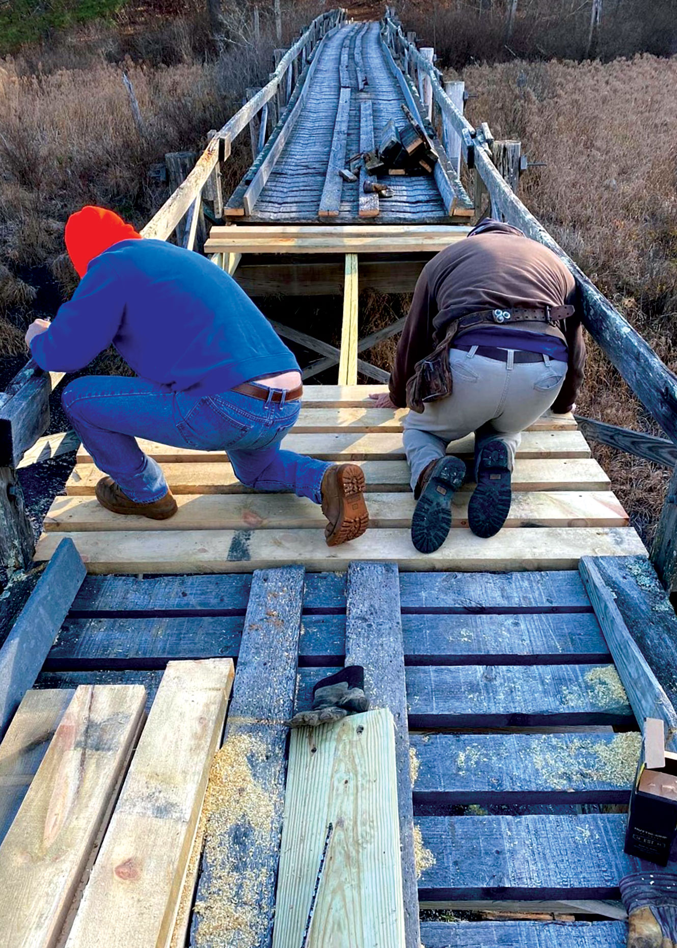 Two men faced away from camera repairing a section of bridge