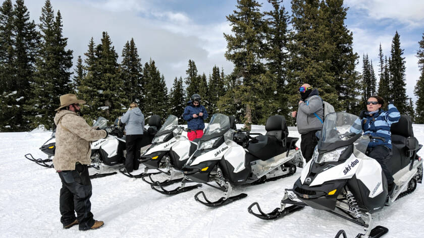 Snowmobilers on snowmobiles with trees in background