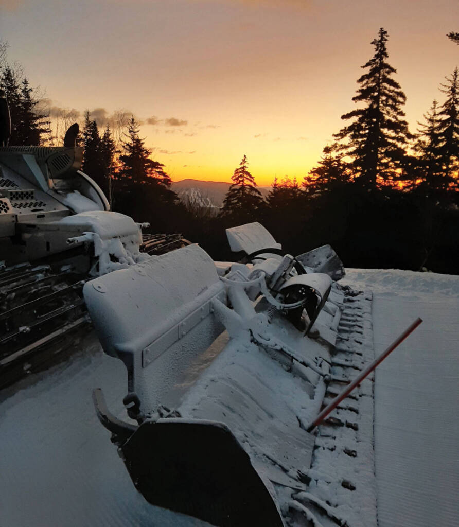 Snow groomer against sunset backdrop