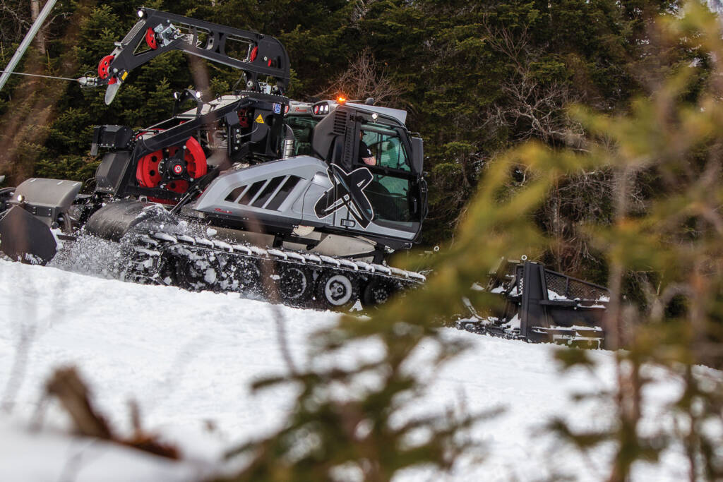 Side view of snow grooming machine with tree branch in foreground