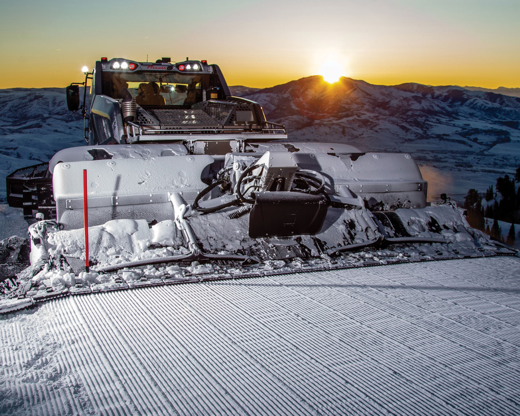 Prinoth snow groomer with sun setting in background