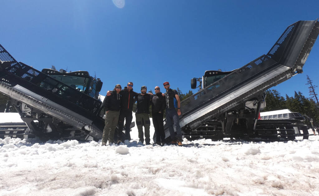 Software team posing for group photo between two snow groomers