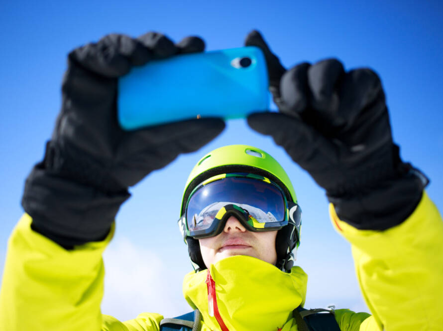 Person in snow suit taking photo or video with mobile phone