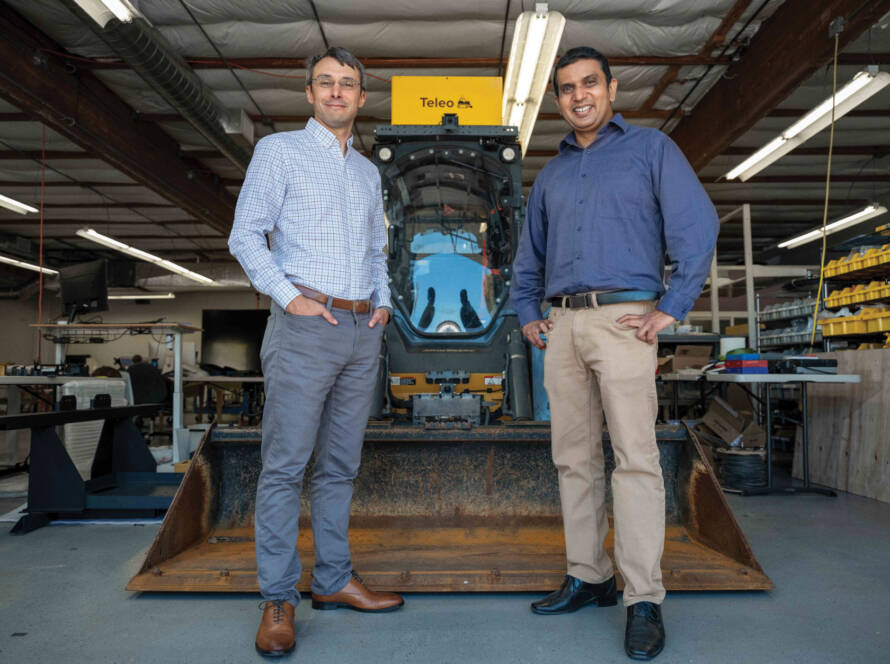 Rom Clément and Vinay Shet posing for photo in front of parked loader